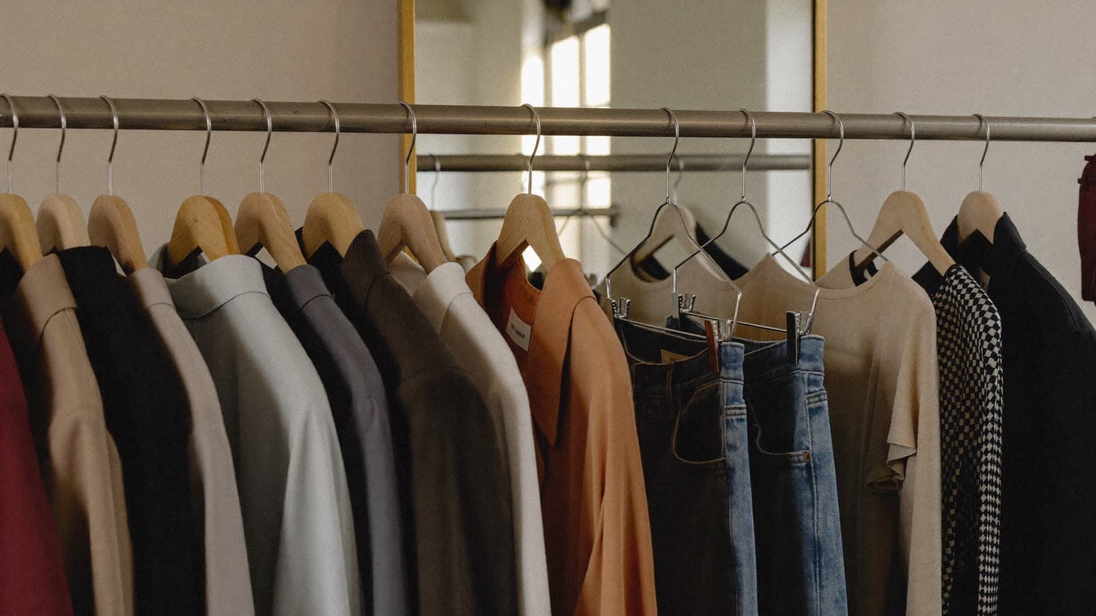 A rail of clothes in every style — suits, silks, denim — in front of a gold-framed mirror