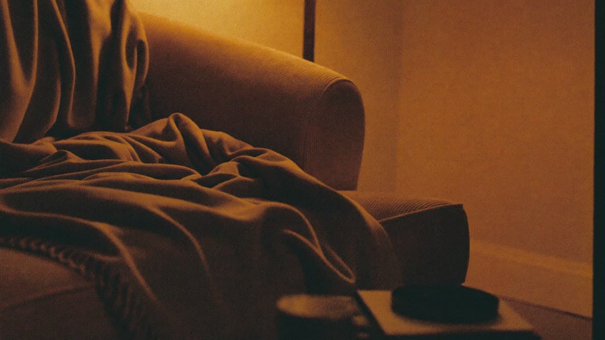 A soft blanket thrown over a corduroy armchair in low amber lamplight