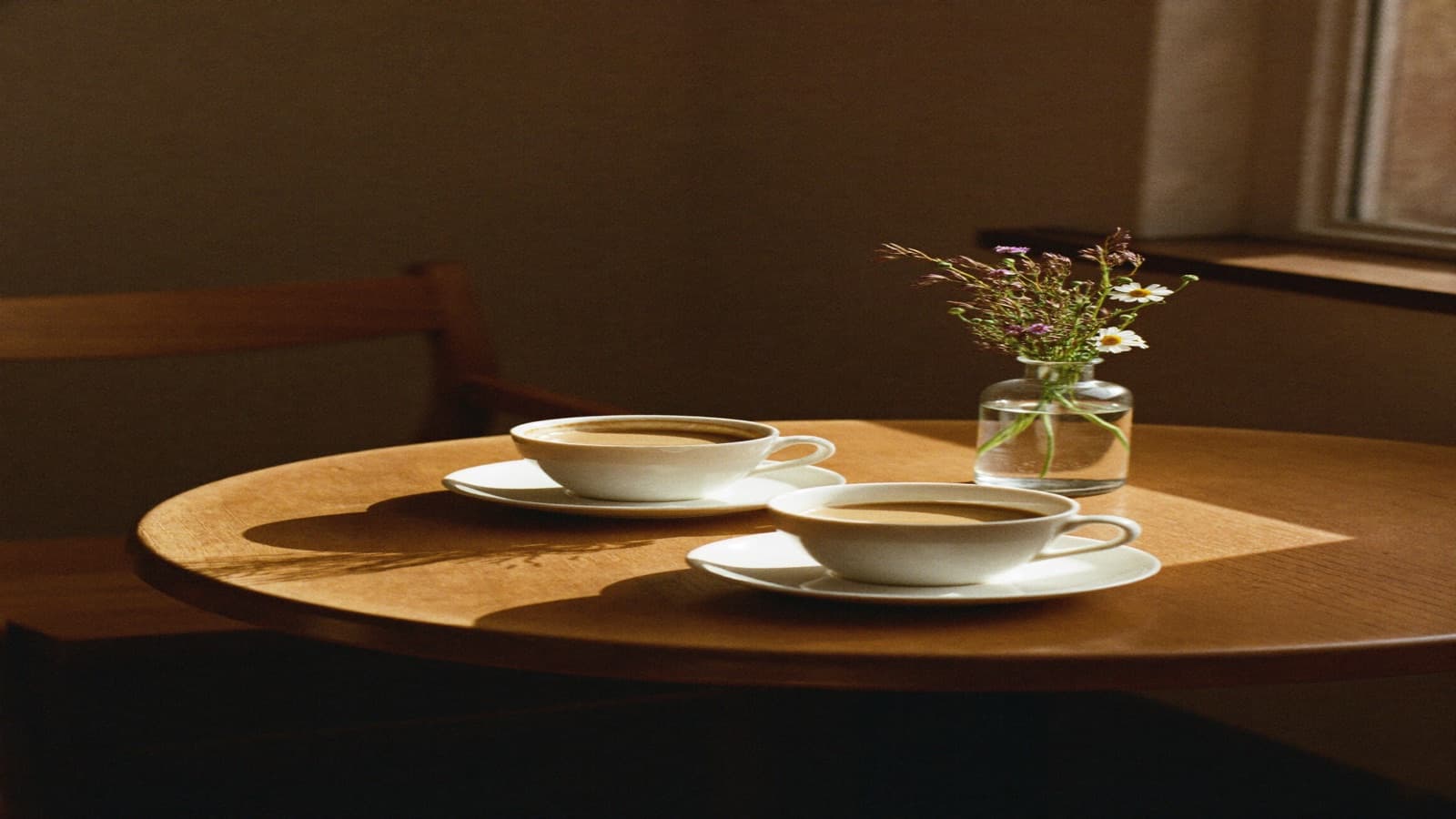 Two cups of tea and a small jar of wildflowers on a sunlit café table