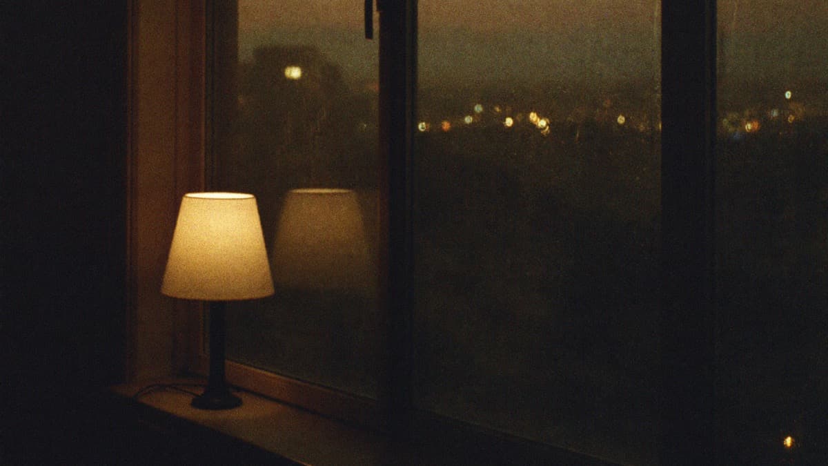 A small lamp glowing on a windowsill at nightfall