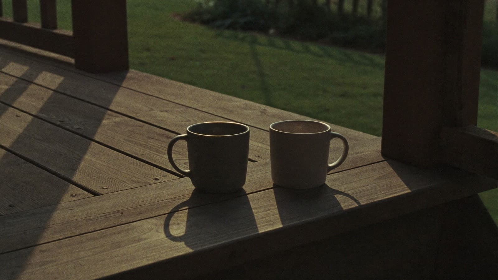 Two mugs side by side on a wooden porch step in low evening light
