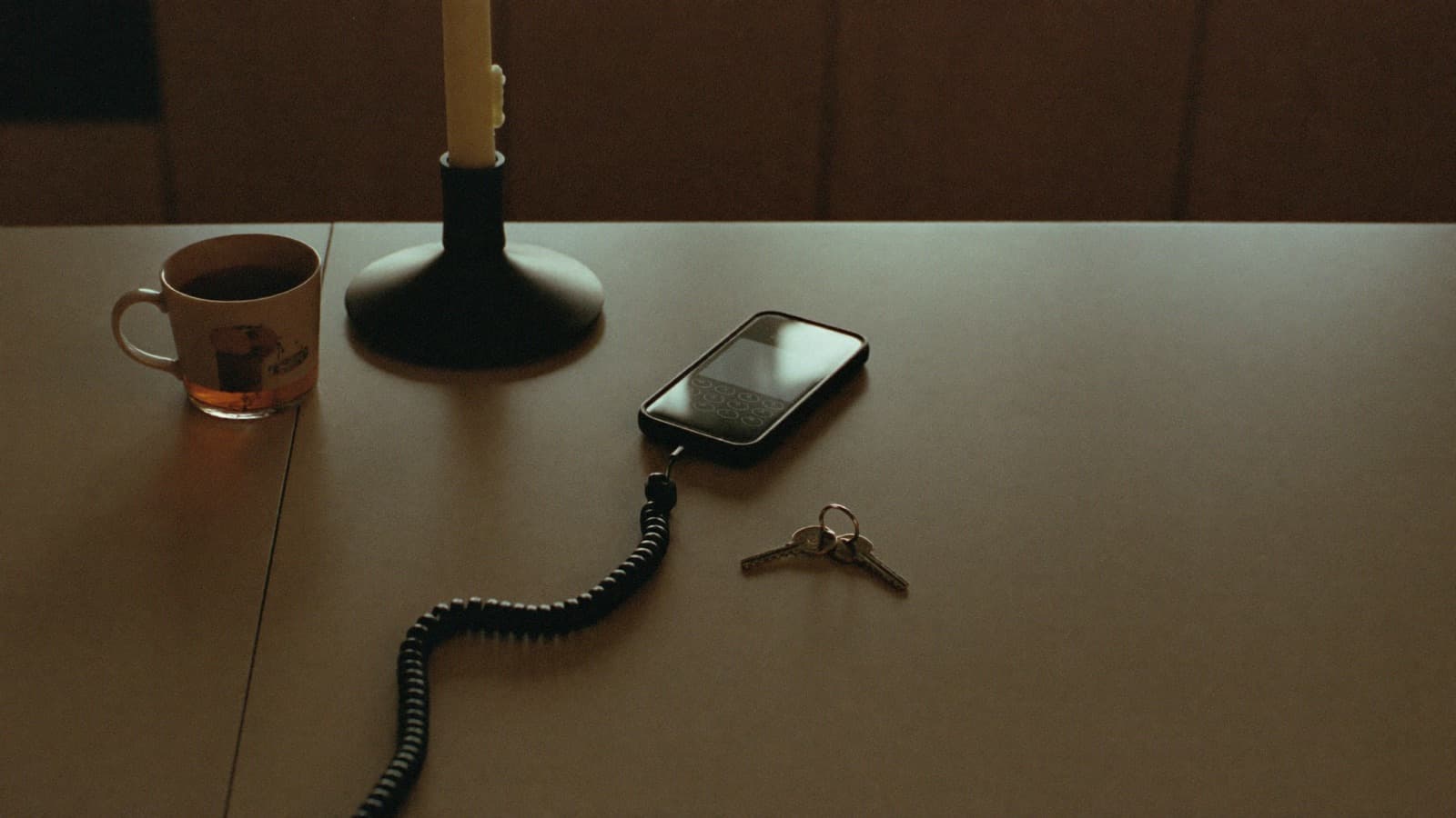 A phone, keys and a mug of tea on a table in low evening light