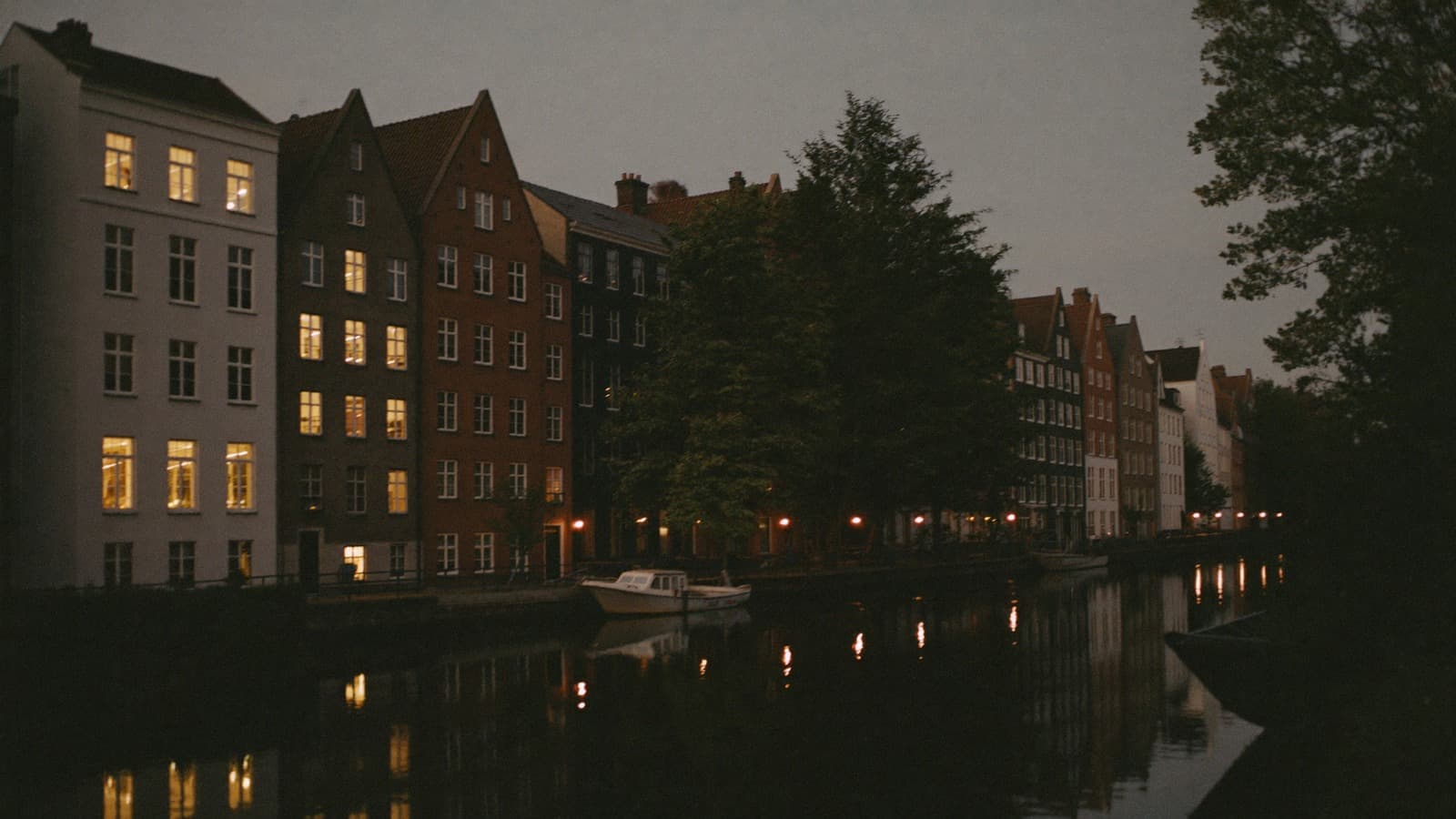A canal at dusk, gabled houses with lit windows along the far bank
