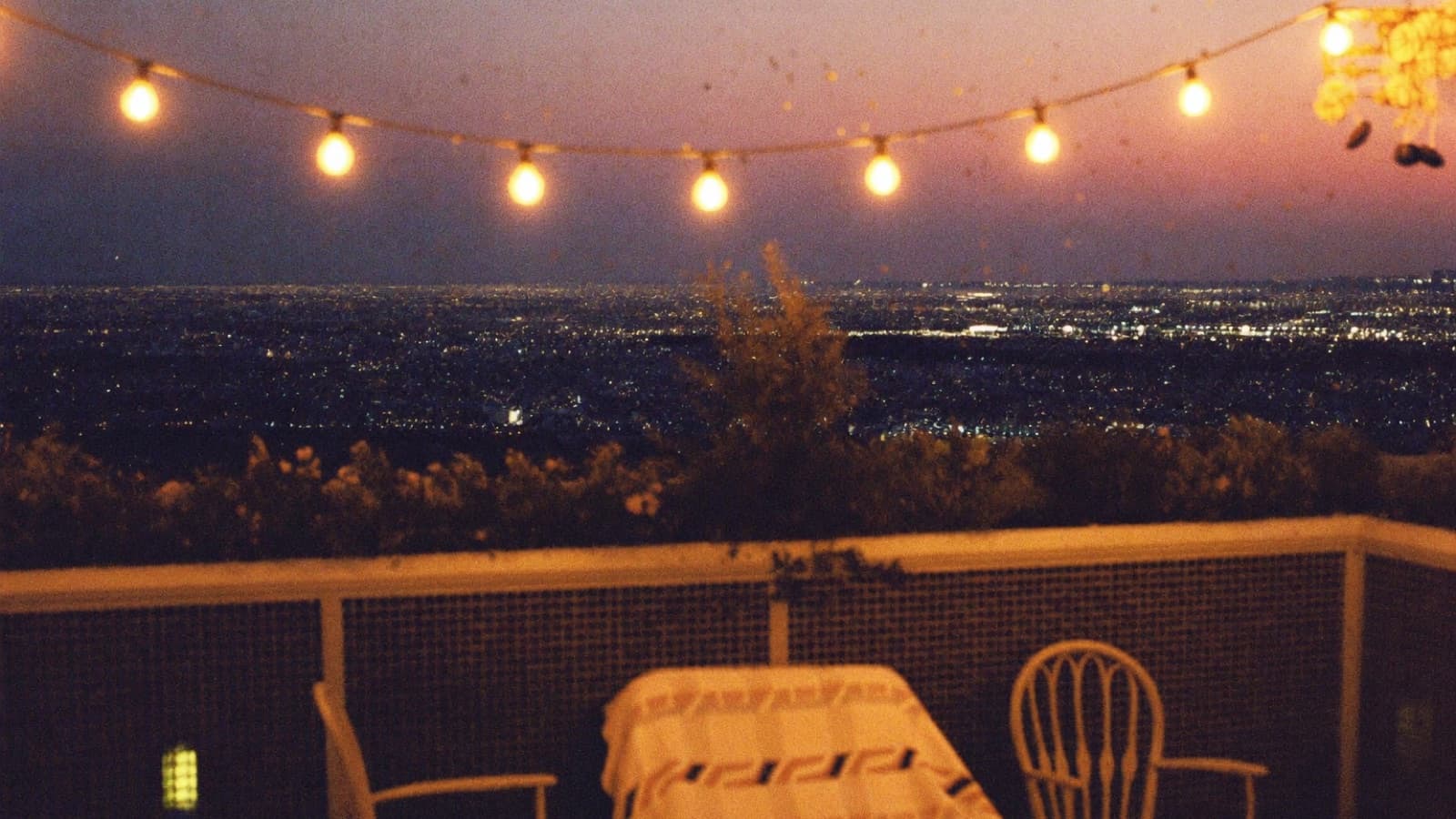 String lights over a terrace, a city glittering below at dusk