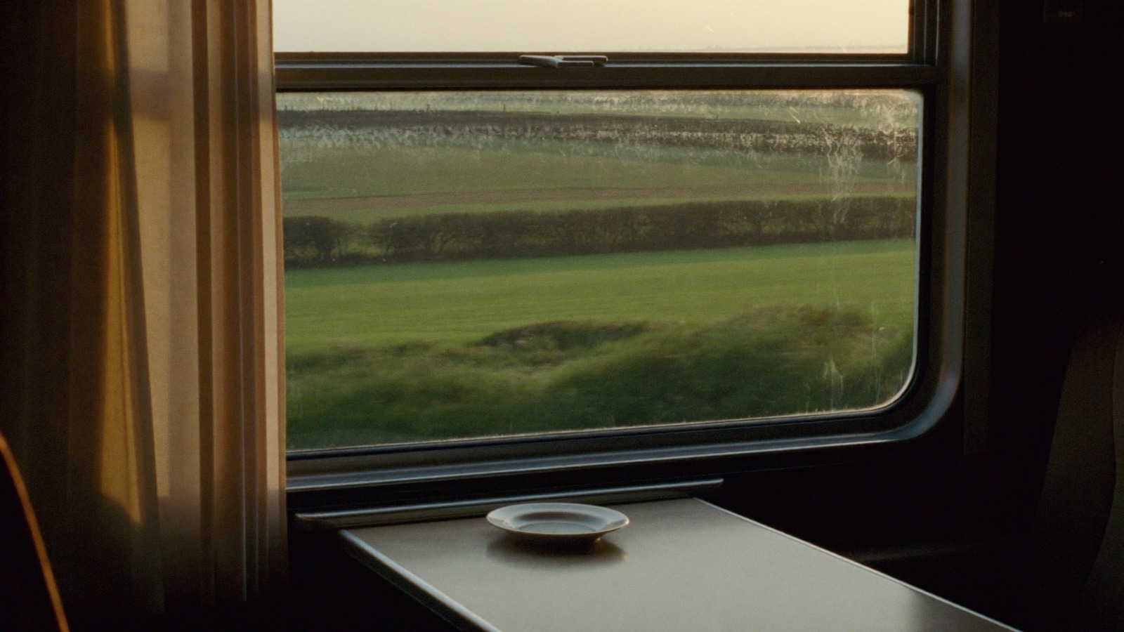 A bare table by a train window, fields and hedgerows passing outside