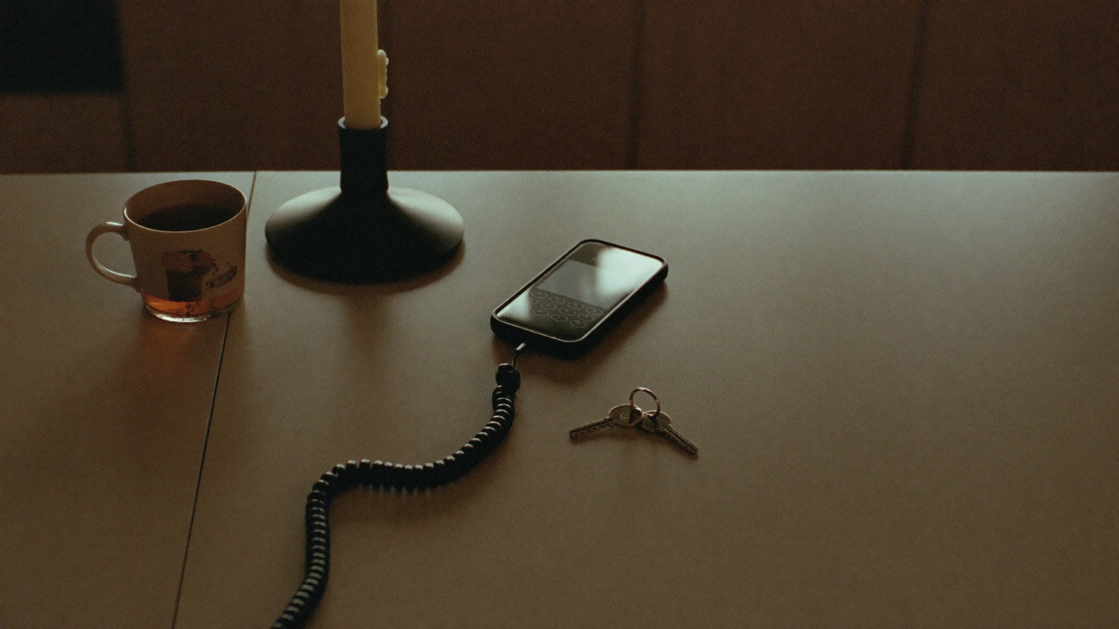 A phone, keys and a mug of tea on a table in low evening light