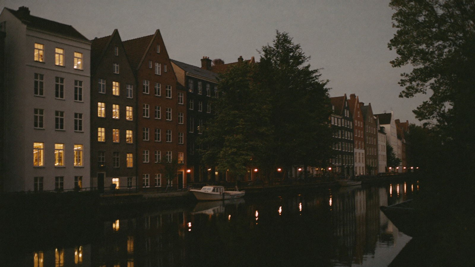 A canal at dusk, gabled houses with lit windows along the far bank
