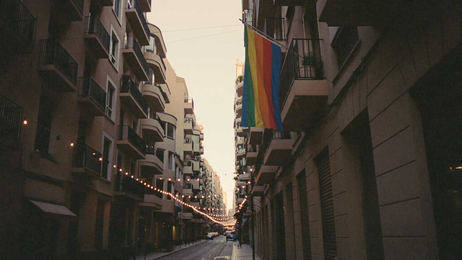 A narrow street hung with a rainbow flag and festoon lights